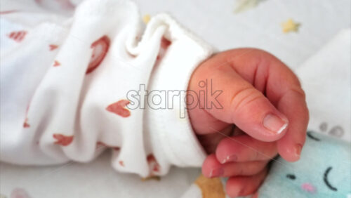 Close up of a newborn baby’s tiny hand clenched in soft natural light while resting - Starpik Stock
