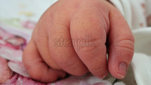 Close up of a newborn baby’s tiny hand clenched in soft natural light while resting - Starpik Stock