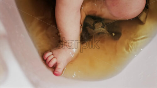 Close up of a newborn’s baby feet submerged in warm bath with the mother’s hand gently touching the infant - Starpik Stock