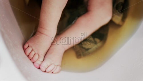 Close up of a newborn’s baby feet submerged in warm bath with the mother’s hand gently touching the infant - Starpik Stock