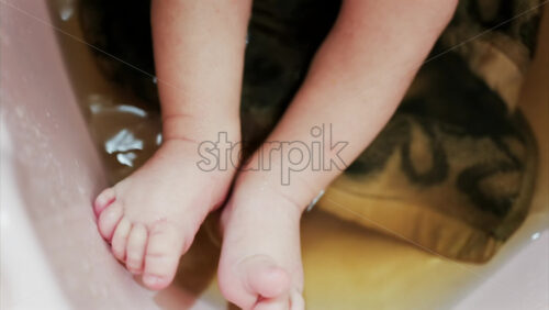 Close up of a newborn’s baby feet submerged in warm bath with the mother’s hand gently touching the infant - Starpik Stock