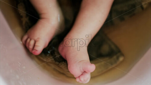 Close up of a newborn’s baby feet submerged in warm bath with the mother’s hand gently touching the infant - Starpik Stock