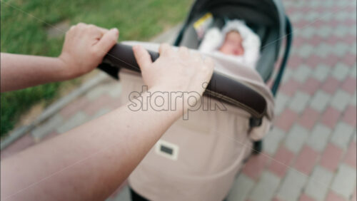 Close up of a parent’s hand pushing a stroller handle while walking in a park - Starpik Stock