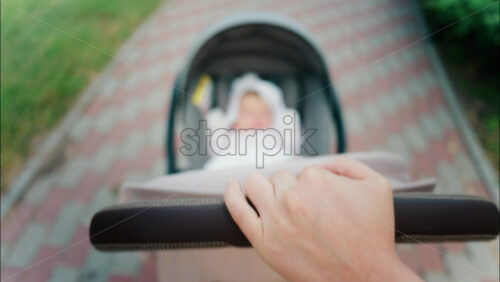 Close up of a parent’s hand pushing a stroller handle while walking in a park - Starpik Stock