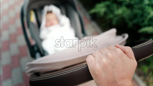 Close up of a parent’s hand pushing a stroller handle while walking in a park - Starpik Stock