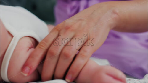 Close up of a parent’s hands massaging a baby’s hands and arms - Starpik Stock