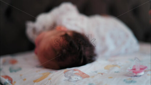 Close up of a pink pacifier with a baby lying down and sleeping peacefully in the background - Starpik Stock