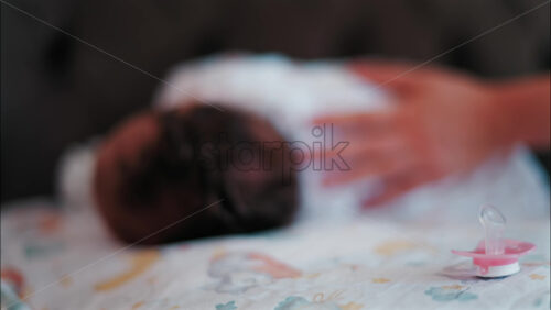 Close up of a pink pacifier with a baby lying down and sleeping peacefully in the background - Starpik Stock