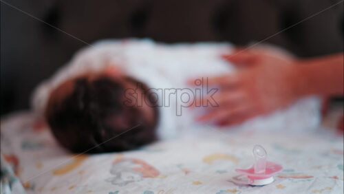 Close up of a pink pacifier with a baby lying down and sleeping peacefully in the background - Starpik Stock