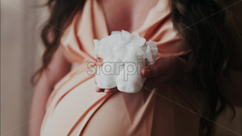 Close up of a pregnant woman holding and playing with white baby socks on her belly - Starpik Stock
