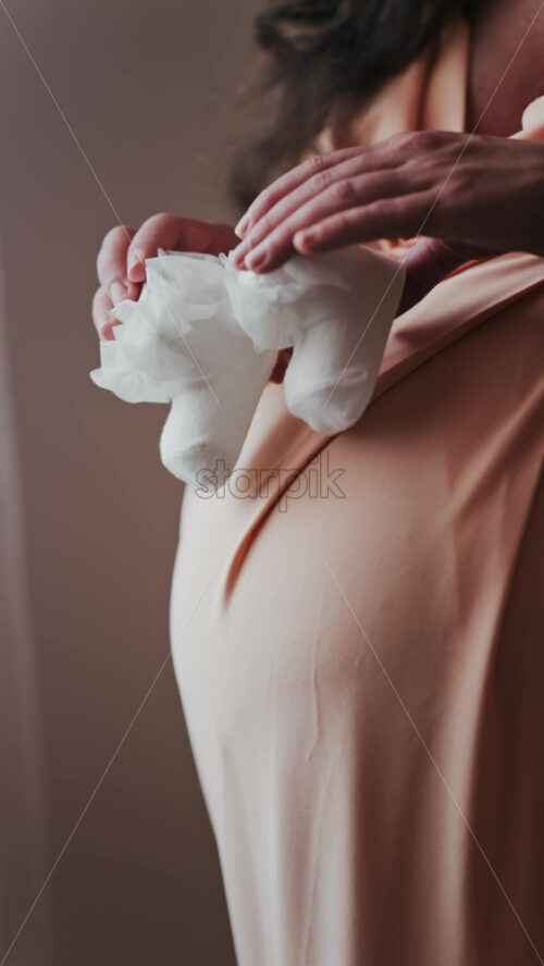 Close up of a pregnant woman holding and playing with white baby socks on her belly. Vertical - Starpik Stock