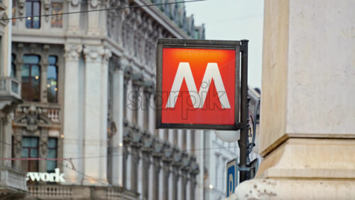 Close up of a red metro sign with a building on the background in Milan, Italy in daylight - Starpik Stock