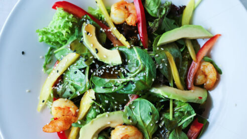 Close up of a salad with spinach, avocado, shrimp, and peppers on a white plate - Starpik Stock