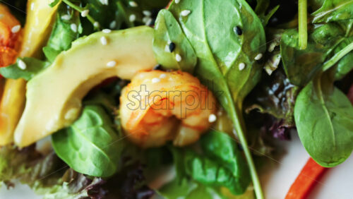 Close up of a salad with spinach, avocado, shrimp, and peppers on a white plate - Starpik Stock
