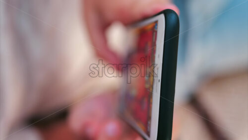 Close up of a smartphone with a cracked screen while a child plays a colourful mobile game. Vertical - Starpik Stock