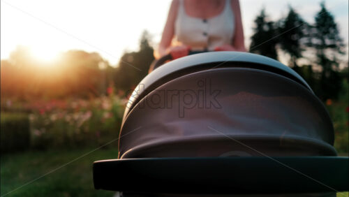 Close up of a stroller being pushed by a mother in the park at sunset - Starpik Stock