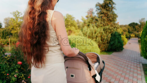 Close up of a stroller being pushed by a mother in the park at sunset - Starpik Stock