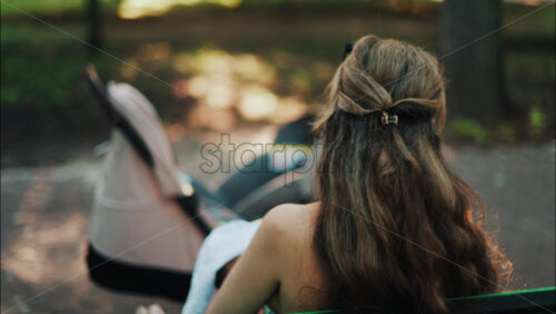 Close up of a stroller with a mother breastfeeding her baby while sitting on a park bench in the background - Starpik Stock