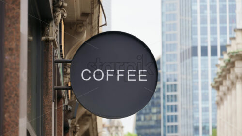 Close-up of a stylish black circular sign with Coffee sign written in white, set against a modern glass office in London, England - Starpik Stock