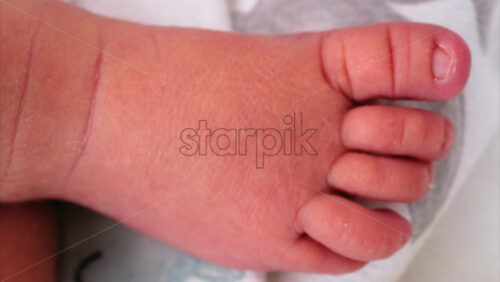 Close up of a the foot of a newborn baby resting on a white bedding with different patterns - Starpik Stock