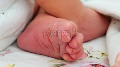 Close up of a the foot of a newborn baby resting on a white bedding with different patterns - Starpik Stock