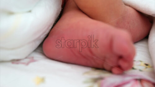 Close up of a the foot of a newborn baby resting on a white bedding with different patterns - Starpik Stock