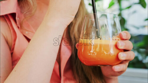 Close up of a woman drinking a glass of orange juice with a black straw - Starpik Stock