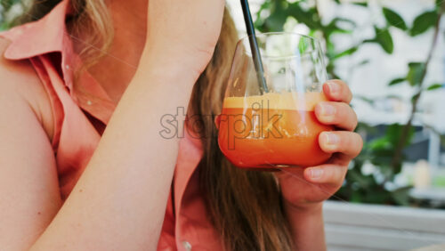 Close up of a woman drinking a glass of orange juice with a black straw - Starpik Stock