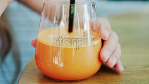 Close up of a woman mixing in a glass of orange juice with a black straw - Starpik Stock
