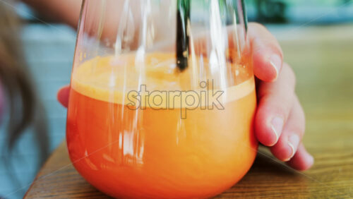 Close up of a woman mixing in a glass of orange juice with a black straw - Starpik Stock