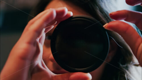 Close up of a woman rotating a camera lens filter near her face - Starpik Stock