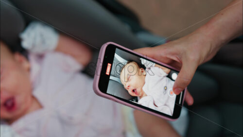 Close up of a woman’s hand capturing a photo of a baby sleeping in a stroller with her smartphone - Starpik Stock
