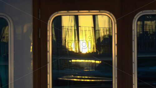 Close-up of a yacht’s window reflecting the golden sunset and marina railings in Cannes - Starpik Stock