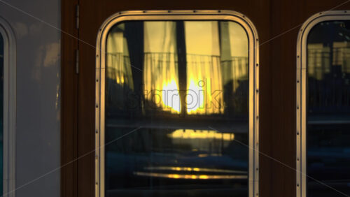 Close-up of a yacht’s window reflecting the golden sunset and marina railings in Cannes - Starpik Stock
