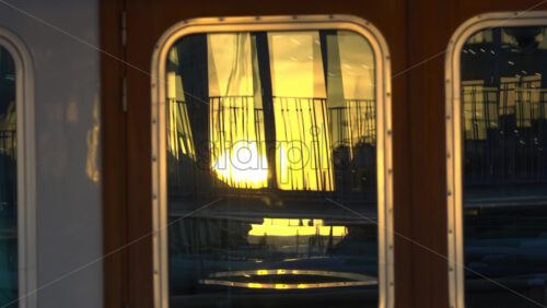 Close-up of a yacht’s window reflecting the golden sunset and marina railings in Cannes - Starpik Stock