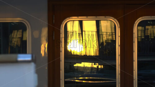 Close-up of a yacht’s window reflecting the golden sunset and marina railings in Cannes - Starpik Stock