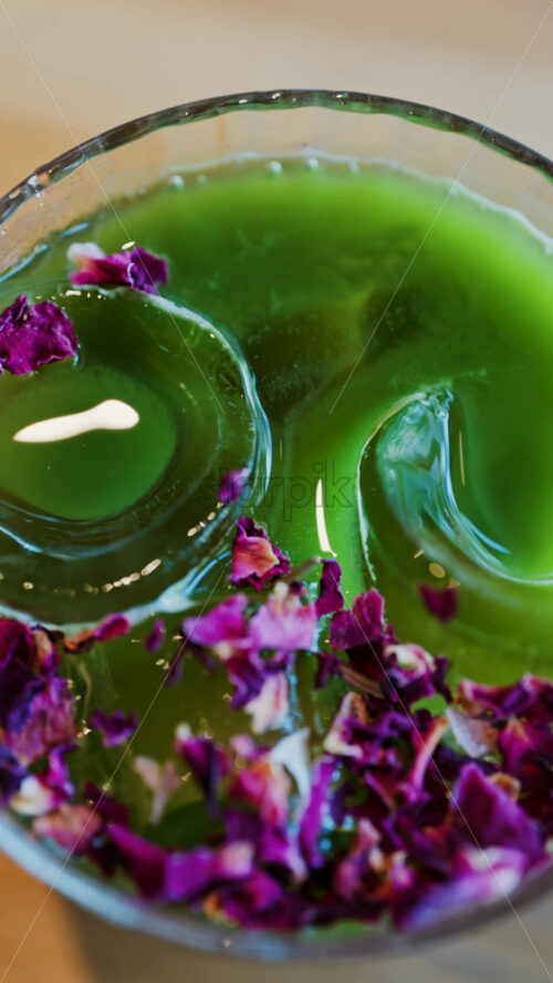Close up of an iced matcha in a glass with purple dried flowers on top. Vertical - Starpik Stock