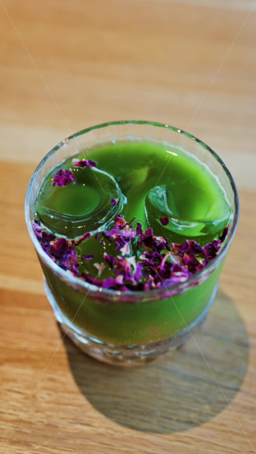 Close up of an iced matcha in a glass with purple dried flowers on top. Vertical - Starpik Stock