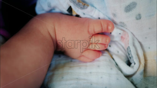 Close up of baby’s foot resting on a patterned blanket with natural light - Starpik Stock