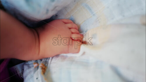 Close up of baby’s foot resting on a patterned blanket with natural light - Starpik Stock