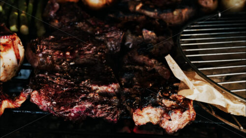 Close up of meats cooking on a grill alongside golden potatoes, asparagus, and garlic - Starpik Stock