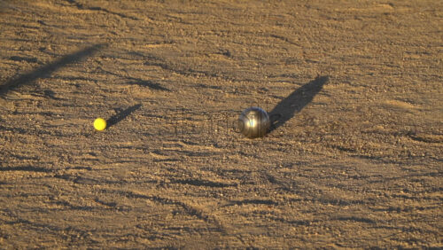 Close-up of petanque balls and jack on a sandy playing field in warm afternoon sunlight - Starpik Stock