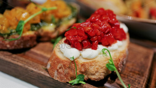 Close up of rustic bruschetta topped with cream cheese and roasted red peppers, garnished with fresh greens - Starpik Stock