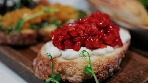 Close up of rustic bruschetta topped with cream cheese and roasted red peppers, garnished with fresh greens - Starpik Stock