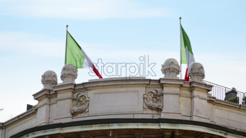 Close up of two Italian flags waving in the wind on top of a building - Starpik Stock