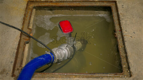 Close-up shot of a sump pump system operating inside a concrete utility pit partially filled with murky water - Starpik Stock