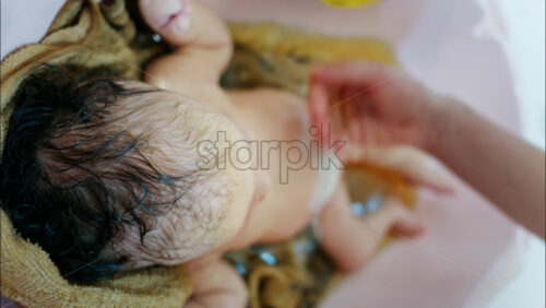 Close up view of a newborn baby being gently bathed by a mother’s hand - Starpik Stock