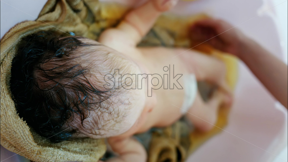 Close up view of a newborn baby being gently bathed by a mother’s hand - Starpik Stock