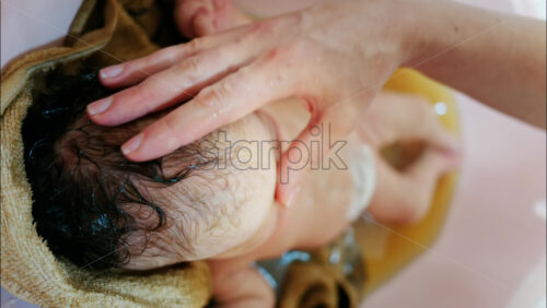 Close up view of a newborn baby being gently bathed by a mother’s hand - Starpik Stock
