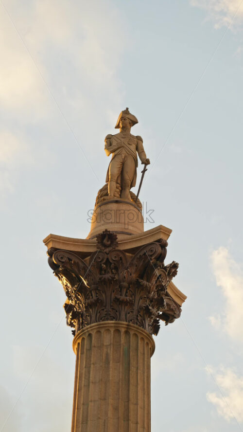 Close-up view of an the towering column of Nelson’s Column in Trafalgar Square, with blue skies and scattered clouds in the background. Vertical, London - Starpik Stock